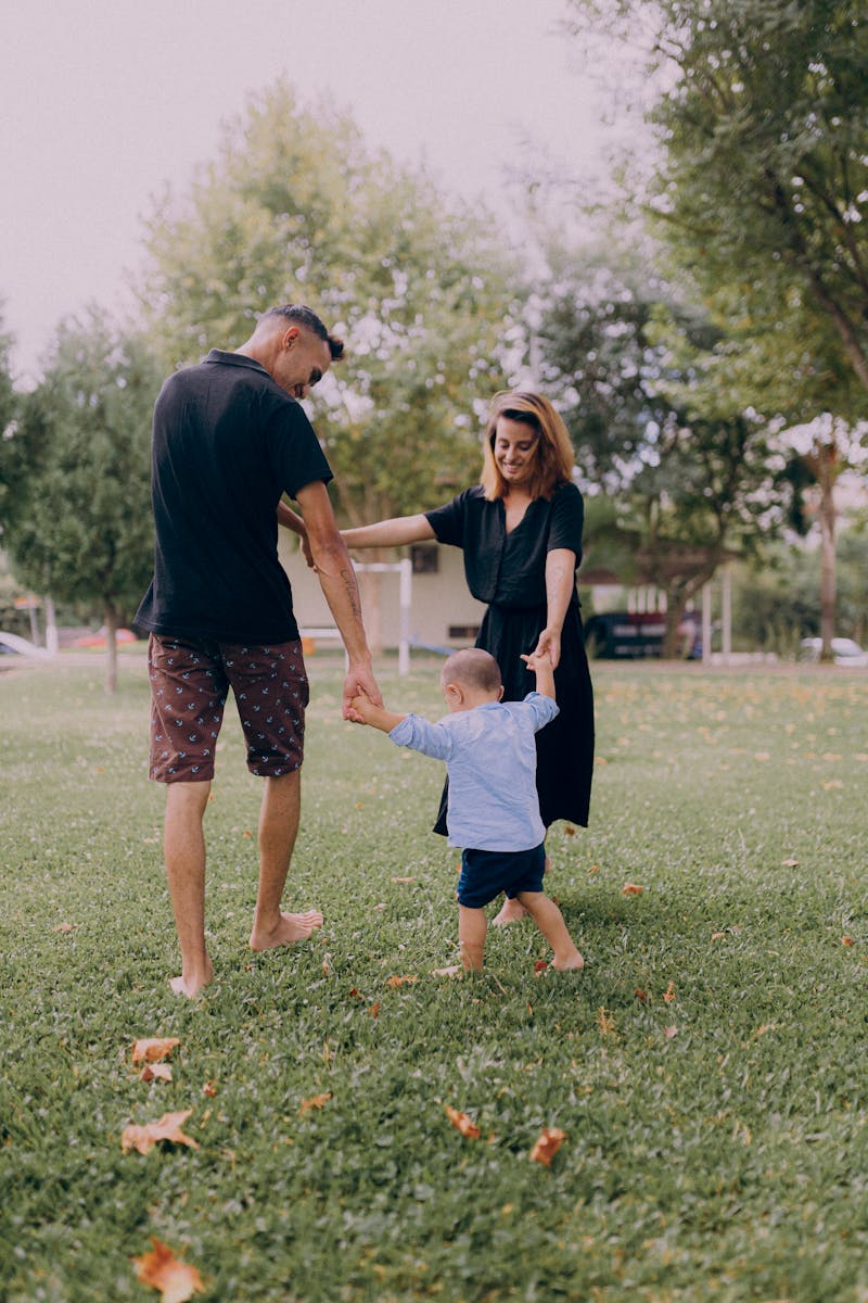 Parents enjoying playtime with their child in a sunny park setting.